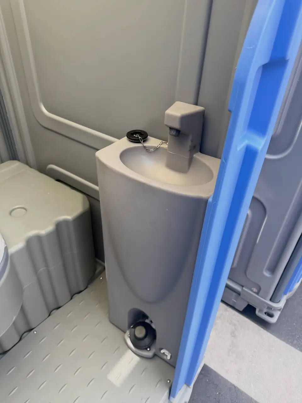 Inside a deluxe porta potty with a sink beside the seat