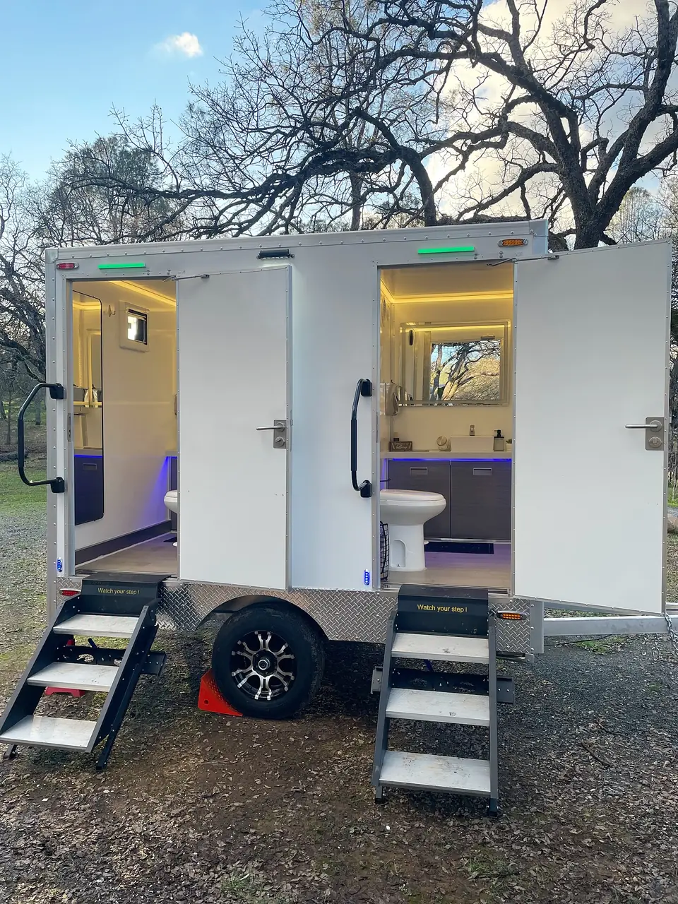 Two-station restroom trailer with both doors open and lit interiors